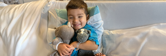Child with cancer smiling while hugging stuffed animals in hospital bed