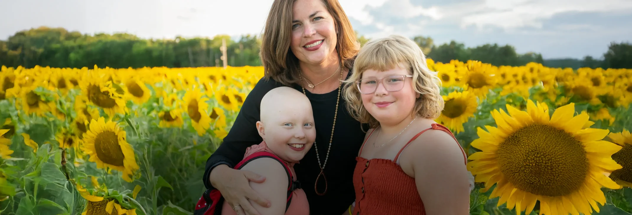 Child affected by cancer and her family posed in a sunflower field